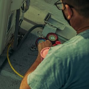 Professional technician repairing an outdoor air conditioning unit with gauges and tools.